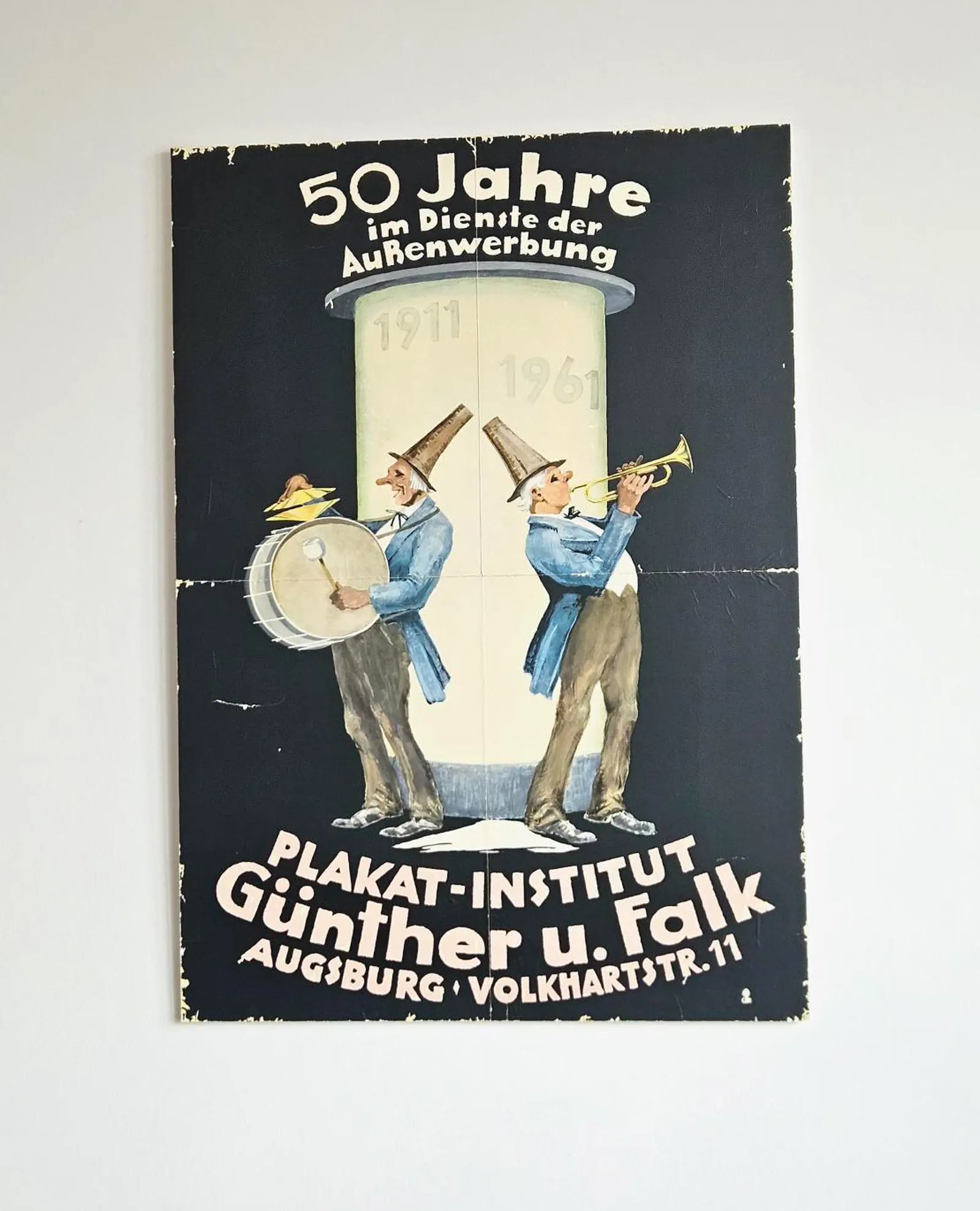 Schild mit dem Aufdruck: "50 Jahre im Dienste der Außenwerbung (1911 - 1961) – Plakatinstitut Günther u. Falk"